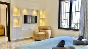 A hotel room with a bed, a sofa, a TV mounted on the wall, and a window with curtains.