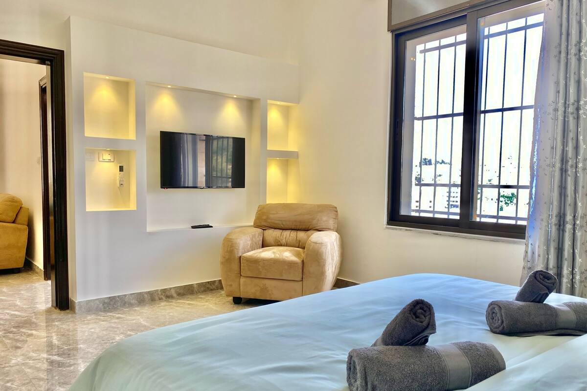 A hotel room with a bed, a sofa, a TV mounted on the wall, and a window with curtains.