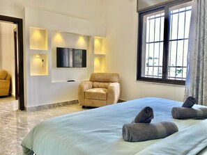 A hotel room with a bed, a sofa, a TV mounted on the wall, and a window with curtains. - Villa Mira Guesthouse - Downtown Amman (Amman)