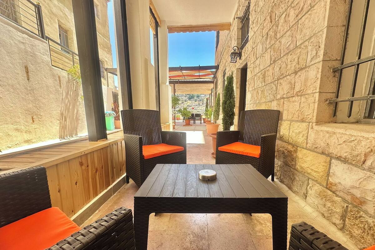 An outdoor seating area with wicker chairs and a table, stone walls, and a view of the street.