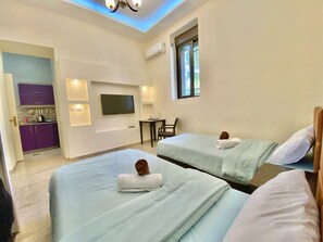 Habitación de hotel con dos camas, televisión, escritorio y una kitchenette pequeña.