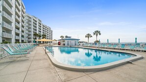 A pool area with lounge chairs and a building with balconies. - Moonspinner by Book That Condo (Panama City Beach)