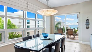A spacious dining area with a glass table and chairs, large windows offering a view of the ocean, and a ceiling light fixture. - Stunning 2 Bedroom Condo with Beach & Pool Access on Siesta Key! (Siesta Key)