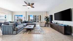A modern living room with a sectional sofa, a coffee table, a TV, and a ceiling fan. - Stunning 2 Bedroom Condo with Beach & Pool Access on Siesta Key! (Siesta Key)