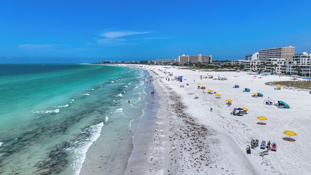 A beach with clear turquoise water, white sand, and several umbrellas. - Stunning 2 Bedroom Condo with Beach & Pool Access on Siesta Key! (Siesta Key)