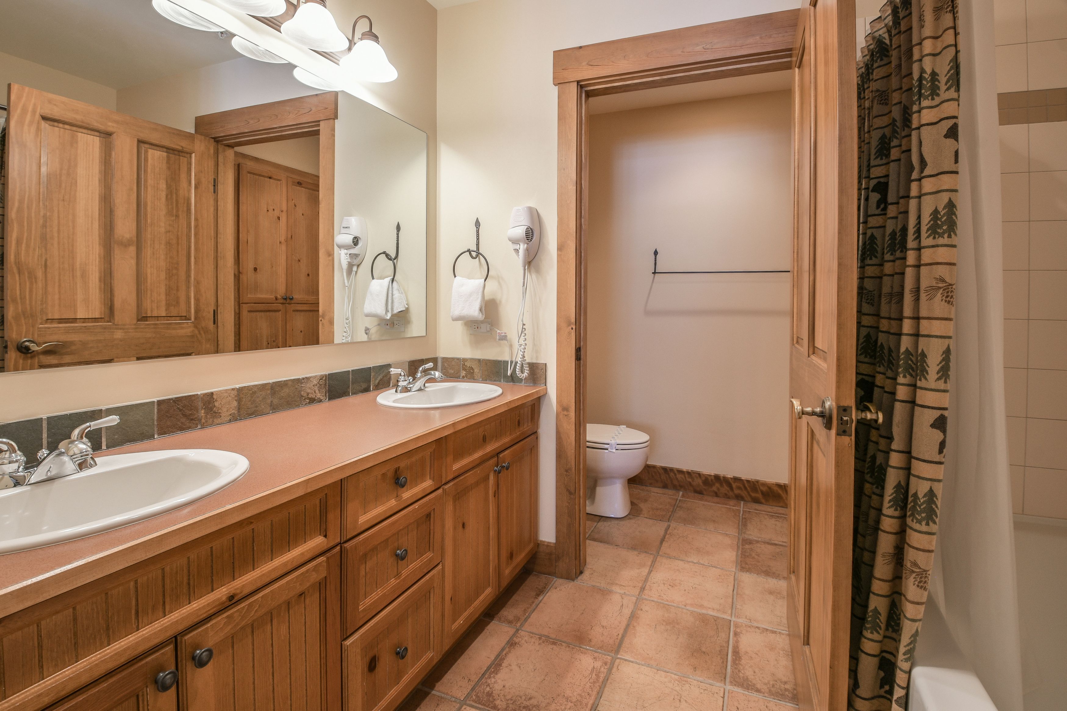 A bathroom with wooden cabinets, a sink, a mirror, a hairdryer, and a toilet.