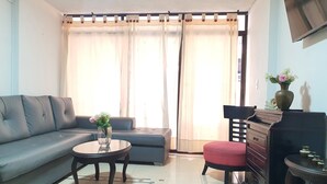 Ein Wohnzimmer mit einer Couch, einem Couchtisch, einem roten Hocker, einem Fernseher und einem Schrank.