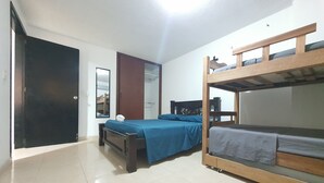 Ein Zimmer mit zwei Etagenbetten, einem Einzelbett, einem Holztisch und einem Spiegel an der Wand.
