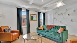 A modern living room with a green sofa, an orange armchair, and a glass coffee table.