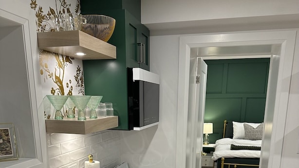A modern kitchen with a white marble countertop, stainless steel sink, and a built-in stove. There is a green accent wall and a wooden shelf above the stove.