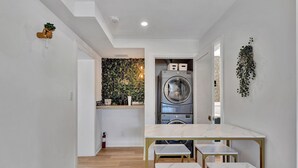 A modern kitchen with a built-in washing machine, a marble countertop, and a small dining area with matching stools.