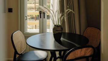 Un comedor con una mesa redonda y dos sillas, una planta en maceta y vistas a través de una ventana con cortinas.