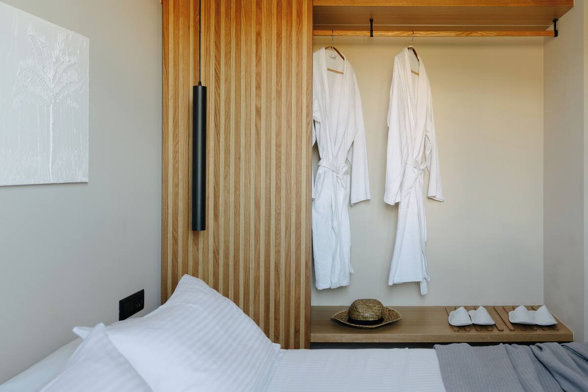 Une chambre à coucher avec un lit, une armoire en bois et une étagère sur laquelle se trouvent un chapeau et des chaussons.