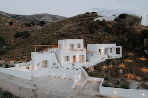 Una villa blanca moderna con un diseño arquitectónico único, con varios niveles y un amplio espacio exterior con vistas a las colinas circundantes.