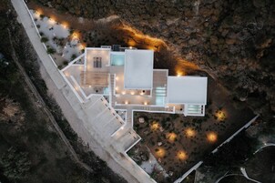 Μια αεροφωτογραφία ενός σύγχρονου σπιτιού με κεντρική αυλή, πολλαπλά επίπεδα και εξωτερικό φωτισμό.