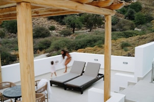 Μια ταράτσα με δύο ξαπλώστρες, ένα τραπέζι και μια ξύλινη πέργκολα.