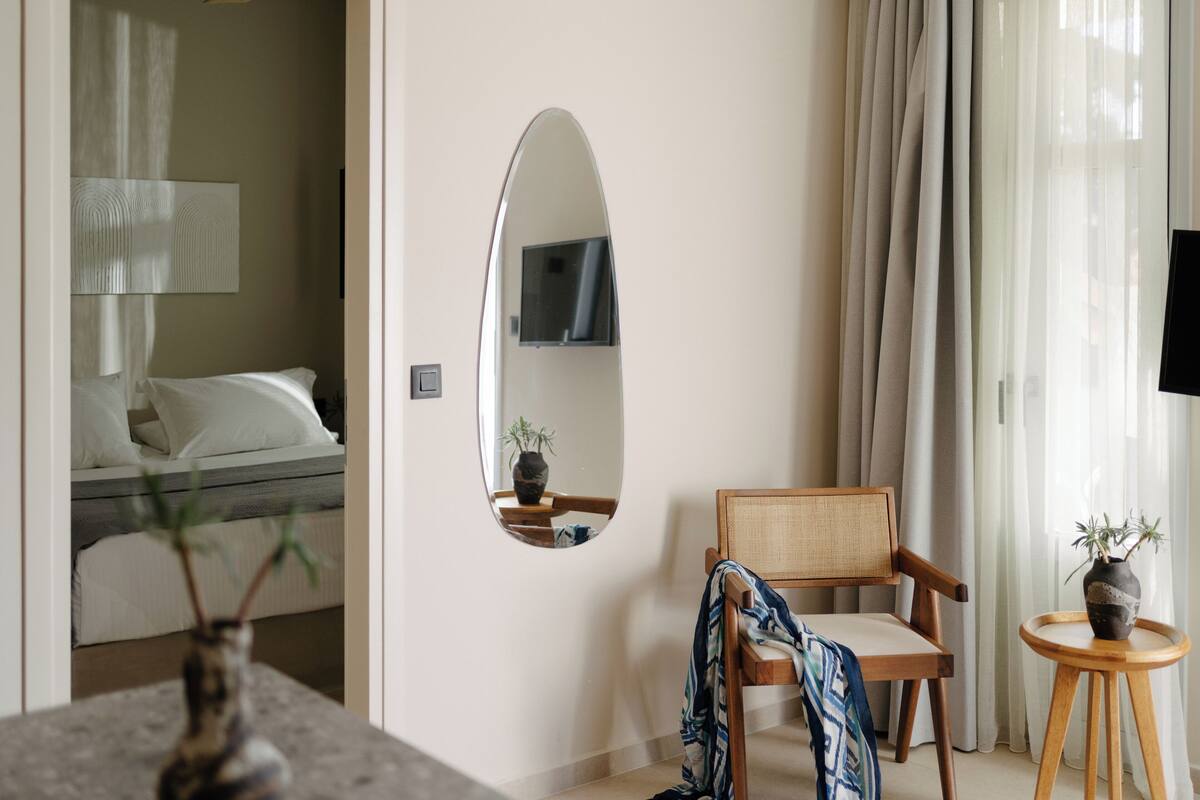 Une chambre d’hôtel avec un lit, une chaise, une petite table avec une plante et un miroir au mur.