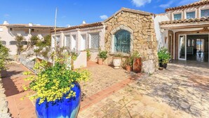 Un patio con un muro de piedra, un jarrón azul grande con flores amarillas y un edificio con techo de tejas.