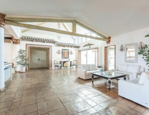 A spacious living area with high ceilings and exposed beams, a dining area with a table and chairs, and a seating area with sofas. - Hotiday Room Collection - Porto Cervo (Arzachena)