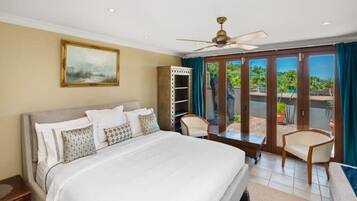 Une chambre dotée d’un grand lit, d’un ventilateur de plafond, d’une armoire et offrant une vue sur une piscine et un espace verdoyant, le tout visible à travers une porte-fenêtre coulissante.
