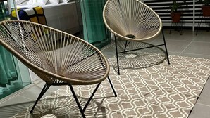 A modern outdoor seating area with two wicker chairs, a patterned rug, and a glass partition. - Pousada Villa Minduba (Japaratinga)