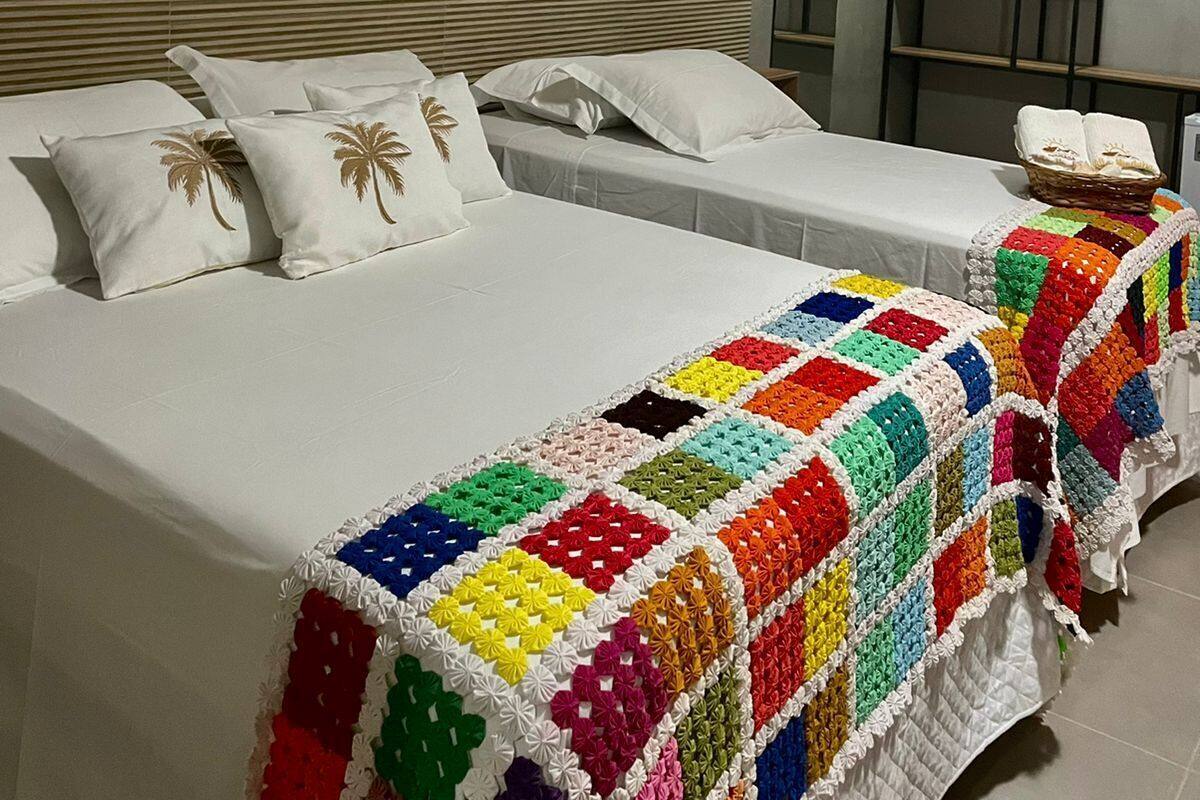 A hotel room with two beds, a colorful blanket, a wall with woven baskets, and a shelf with a basket.