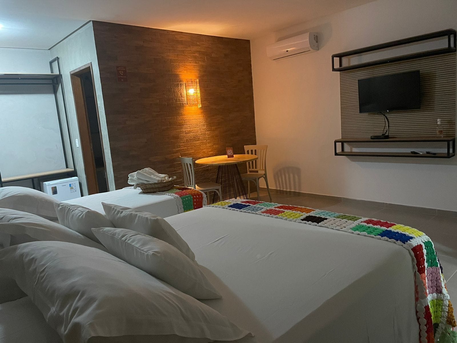 Habitación de hotel con dos camas, una mesita con sillas, un televisor montado en la pared y un equipo de aire acondicionado.