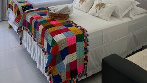 A bedroom with two beds, a colorful crochet blanket, a wooden headboard, and a framed picture of a boat on a beach. - Pousada Villa Minduba (Japaratinga)