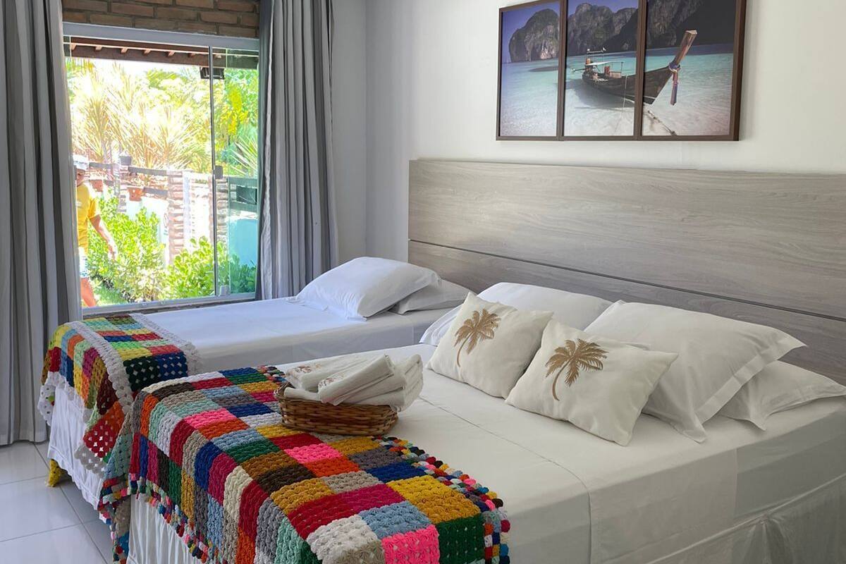 A bedroom with two beds, a colorful crochet blanket, a wooden headboard, and a framed picture of a boat on a beach.
