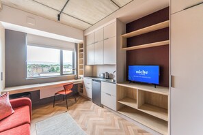 A modern kitchen with a built-in dishwasher, a large window offering a city view, and a flat-screen TV on a wooden shelf.