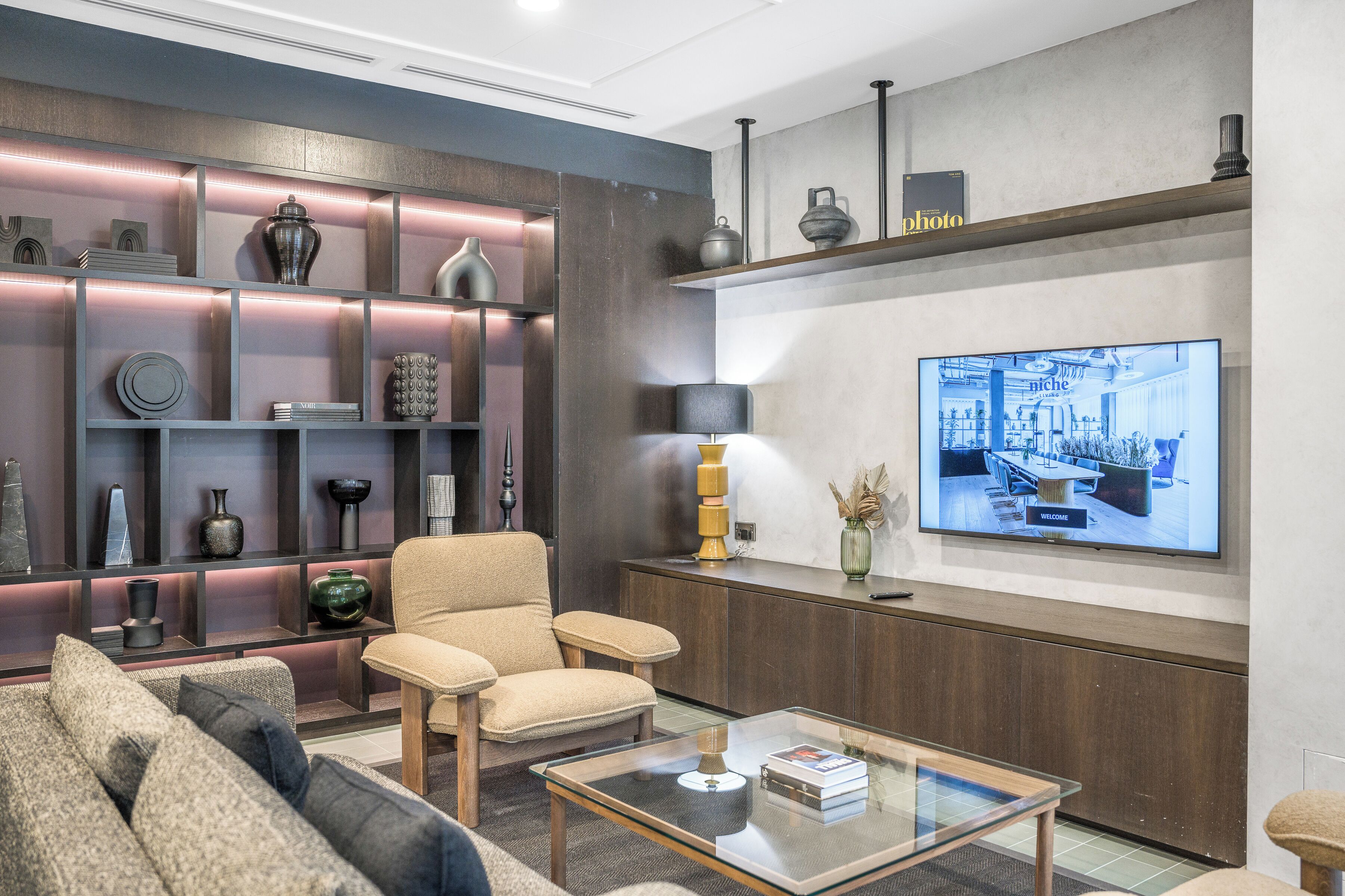 A modern living room with a sofa, armchair, coffee table, and a TV mounted on the wall.