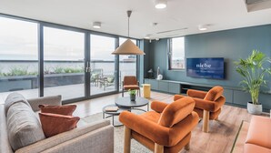 A modern living room with a large window, a sofa, two armchairs, a coffee table, and a television. - Niche Living Rathmines (Dublin)