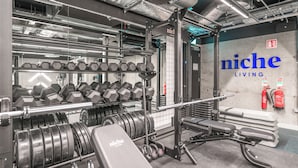 A gym with weightlifting equipment, dumbbells, and a wall with 'niche living' signage. - Niche Living Rathmines (Dublin)