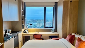 A hotel room with a bed, desk, and window with a city view. - Niche Living Rathmines (Dublin)