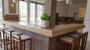 A kitchen with a central island, bar stools, a clock on the wall, and a potted plant. - Villa Rocher - Residence 2 (Fond du Sac)