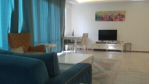A living room with a sofa, a coffee table, a TV, a dining table with chairs, and a painting on the wall. - vbasuıten (Istanbul)