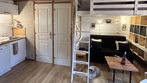 Une pièce compacte et bien éclairée, avec un lit superposé, un petit coin cuisine et un plancher en bois.