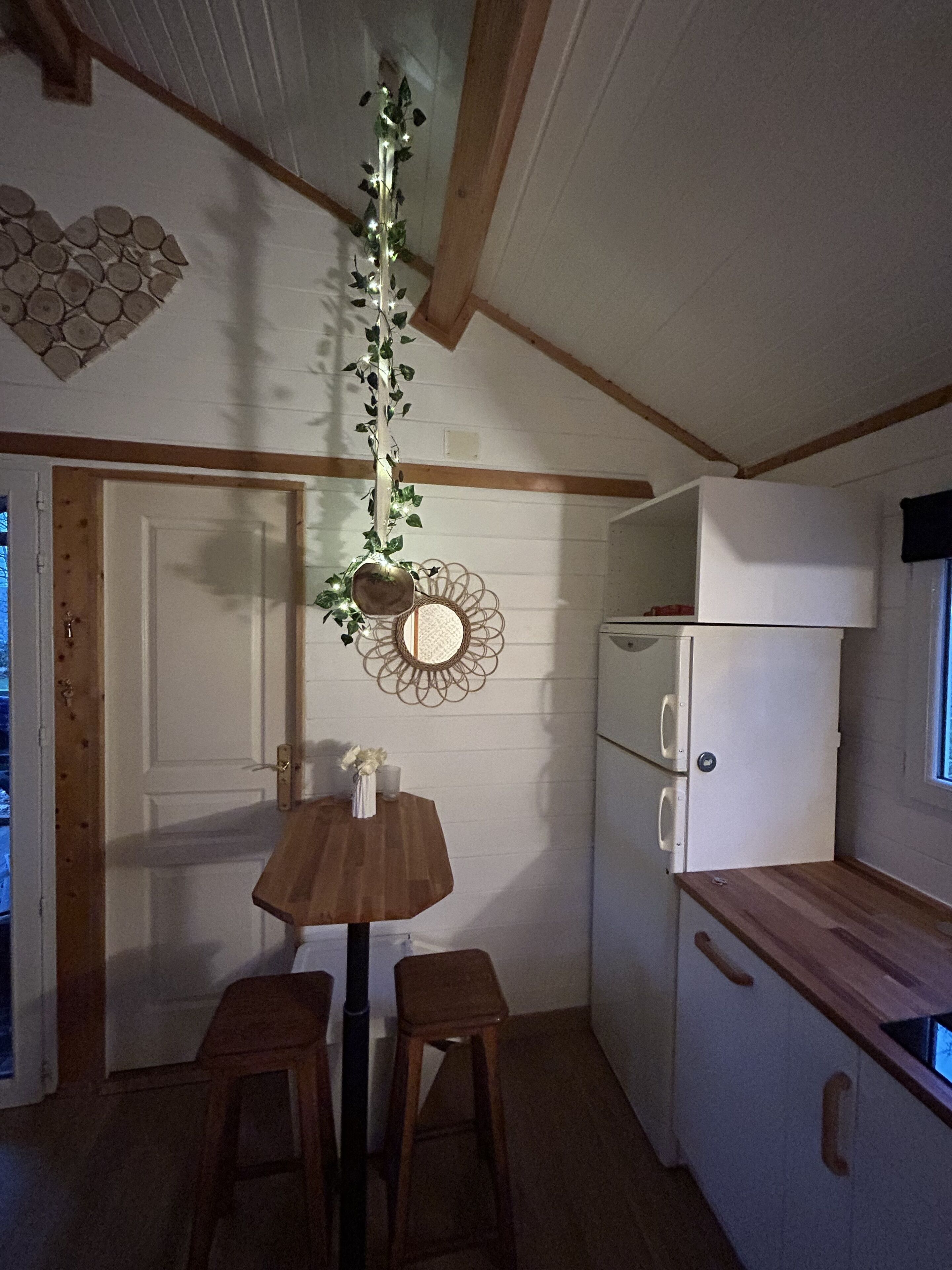 A compact kitchen with a wooden table and stools, a white refrigerator, and a decorative wall hanging.