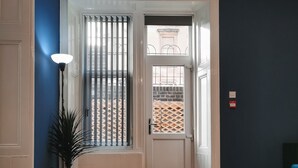 A room with a wooden floor, a black table with a decorative bowl, a blue chair, a potted plant, and a door leading to an outdoor area with a view of a building. - SH Apartments - Dixon Street (Glasgow)