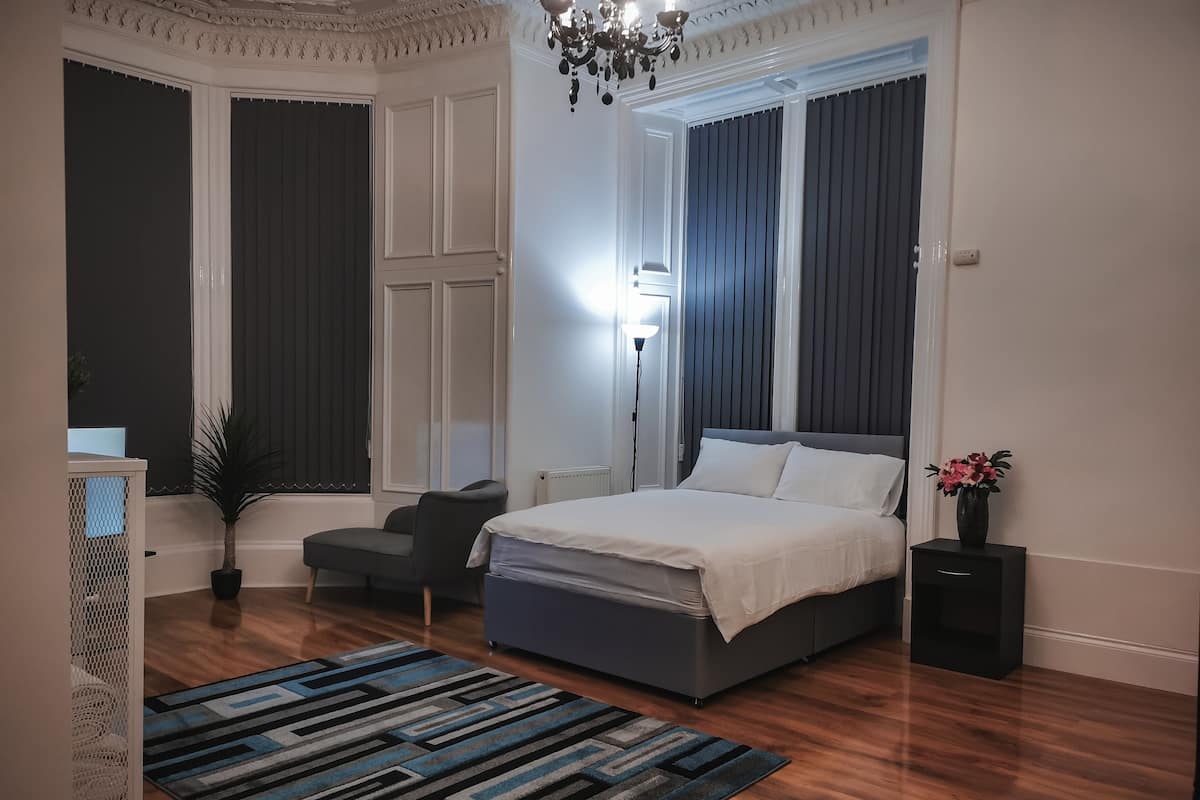 A bedroom with a bed, a desk, a chair, a potted plant, and a window with curtains.
