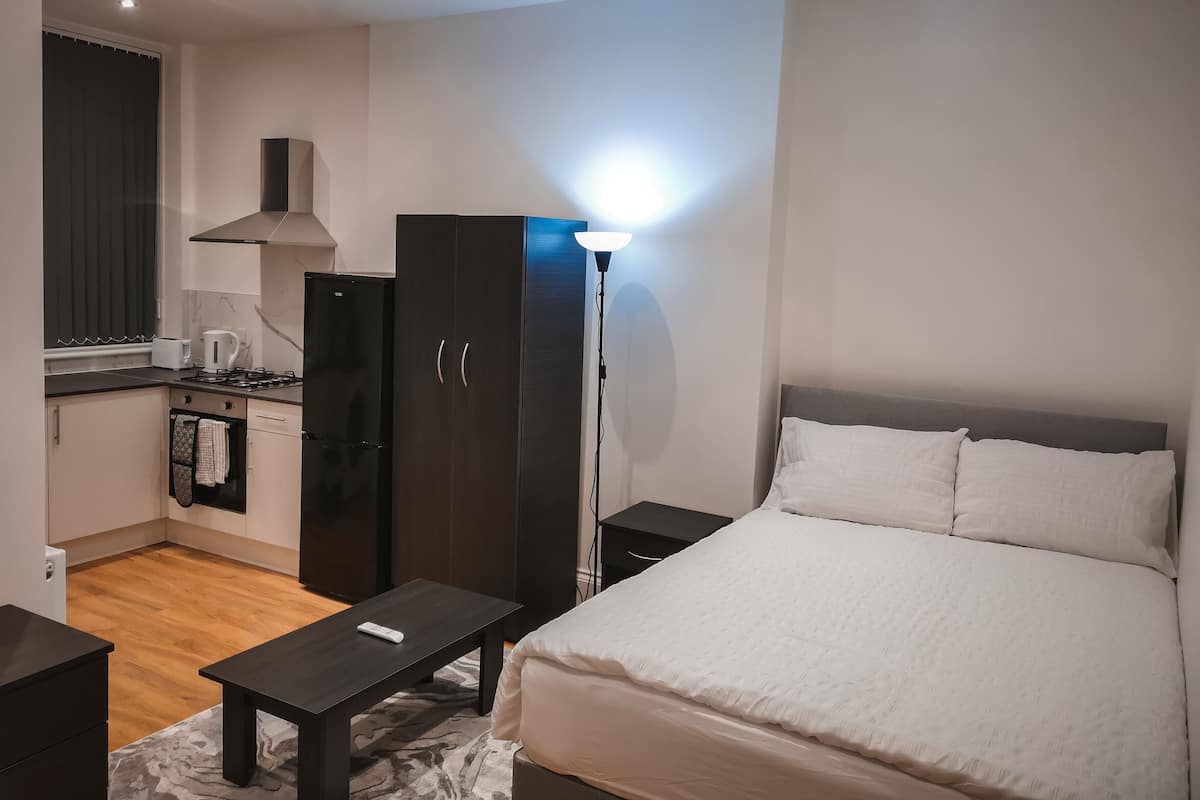 A bedroom with a bed, bedside tables, a wardrobe, a desk, and a kitchenette.
