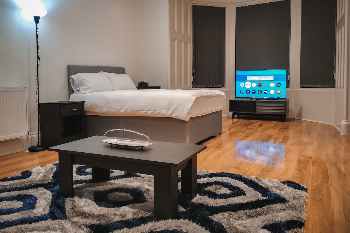 A modern bedroom with a bed, bedside table, lamp, TV, and a patterned rug.