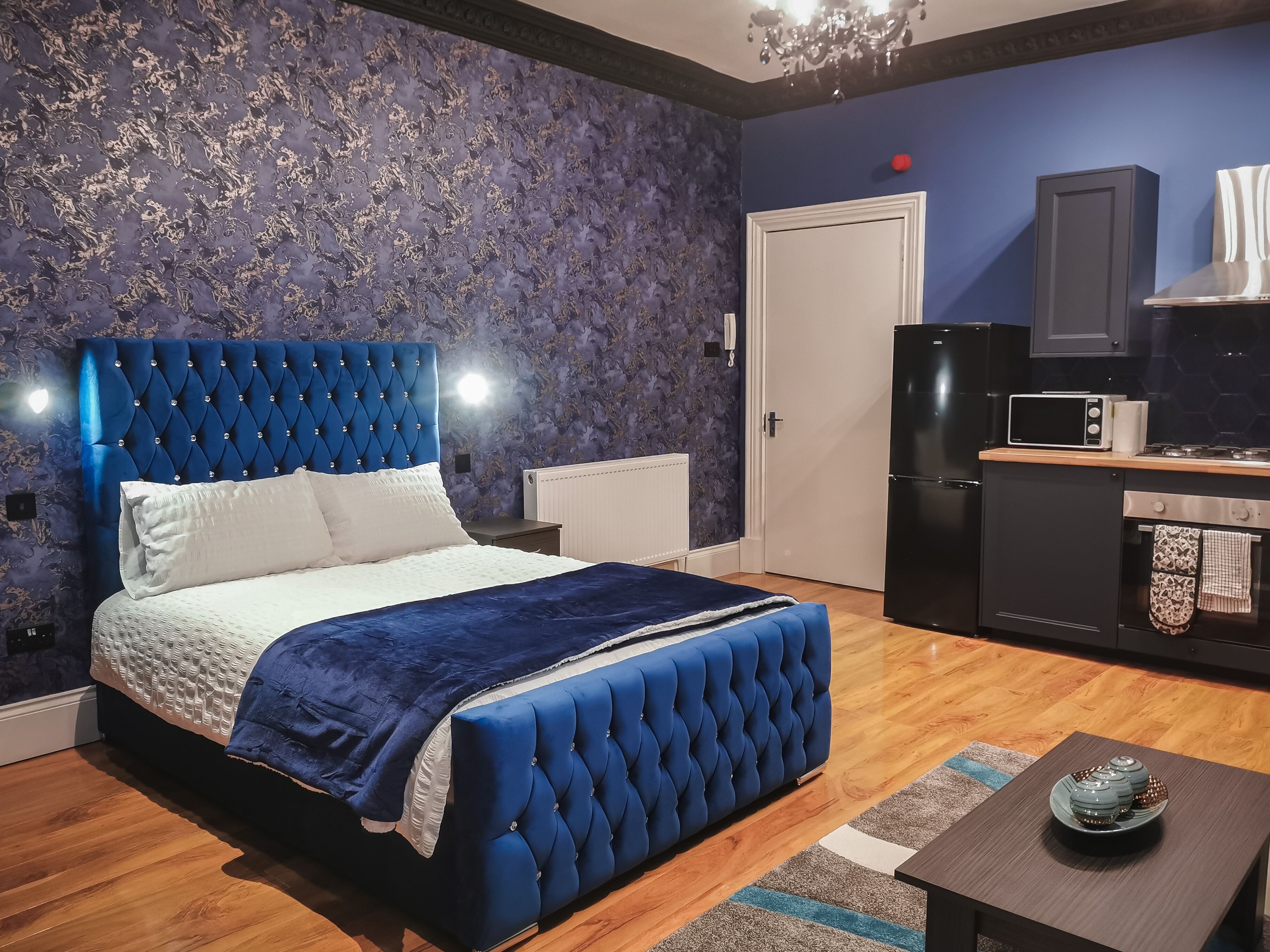 A bedroom with a large bed, a nightstand, a dresser, a microwave, and a refrigerator.