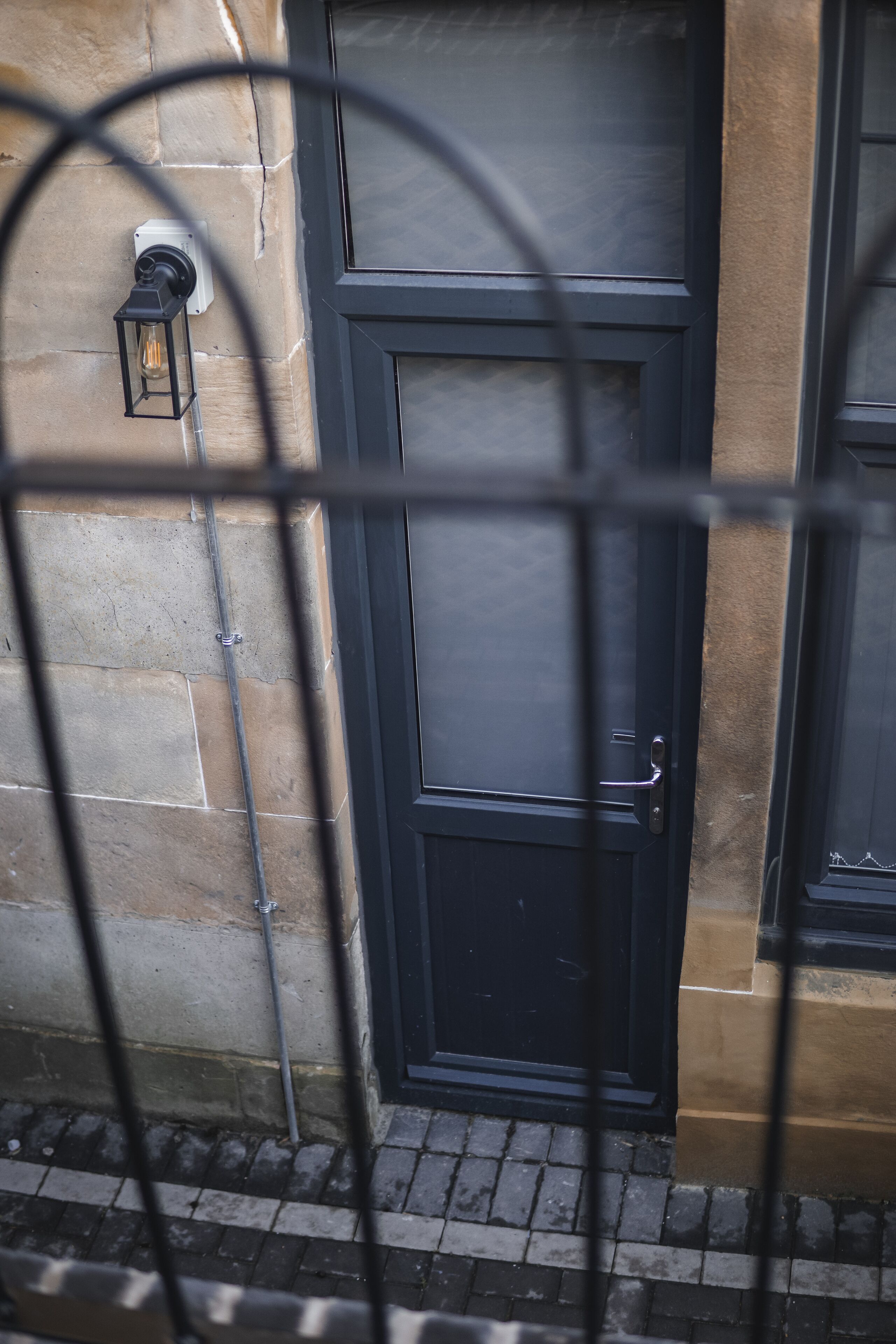 A black door with a light fixture on the wall to the left.