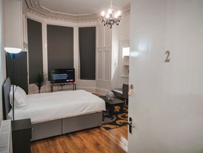 Ein Schlafzimmer mit einem Bett, einem Schreibtisch, einem Fernseher, einer Chandelüster und einer Tür mit einer Nummer.