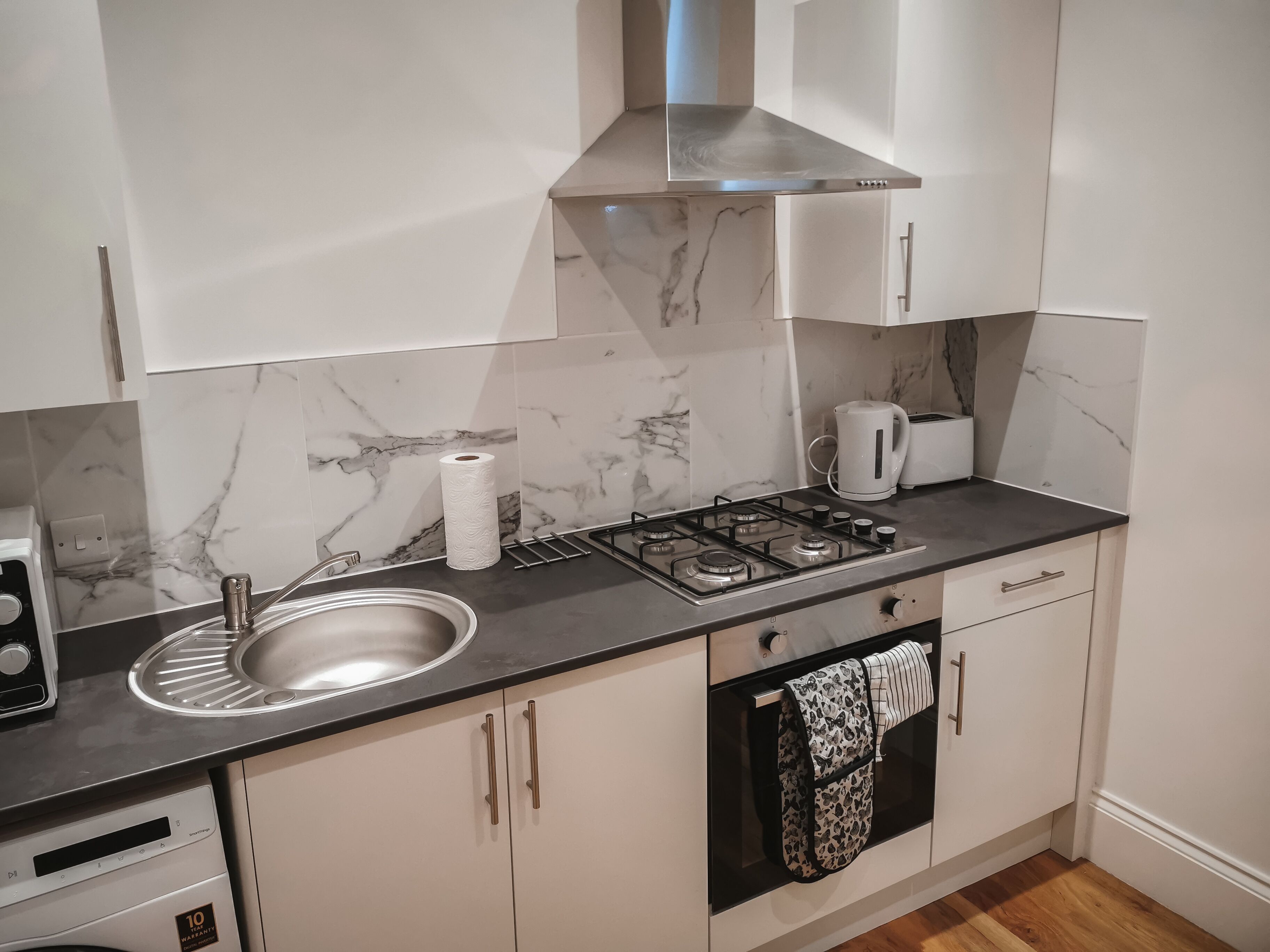 A modern kitchen with white cabinets, a marble backsplash, a stainless steel sink, a gas stove, and a coffee maker.