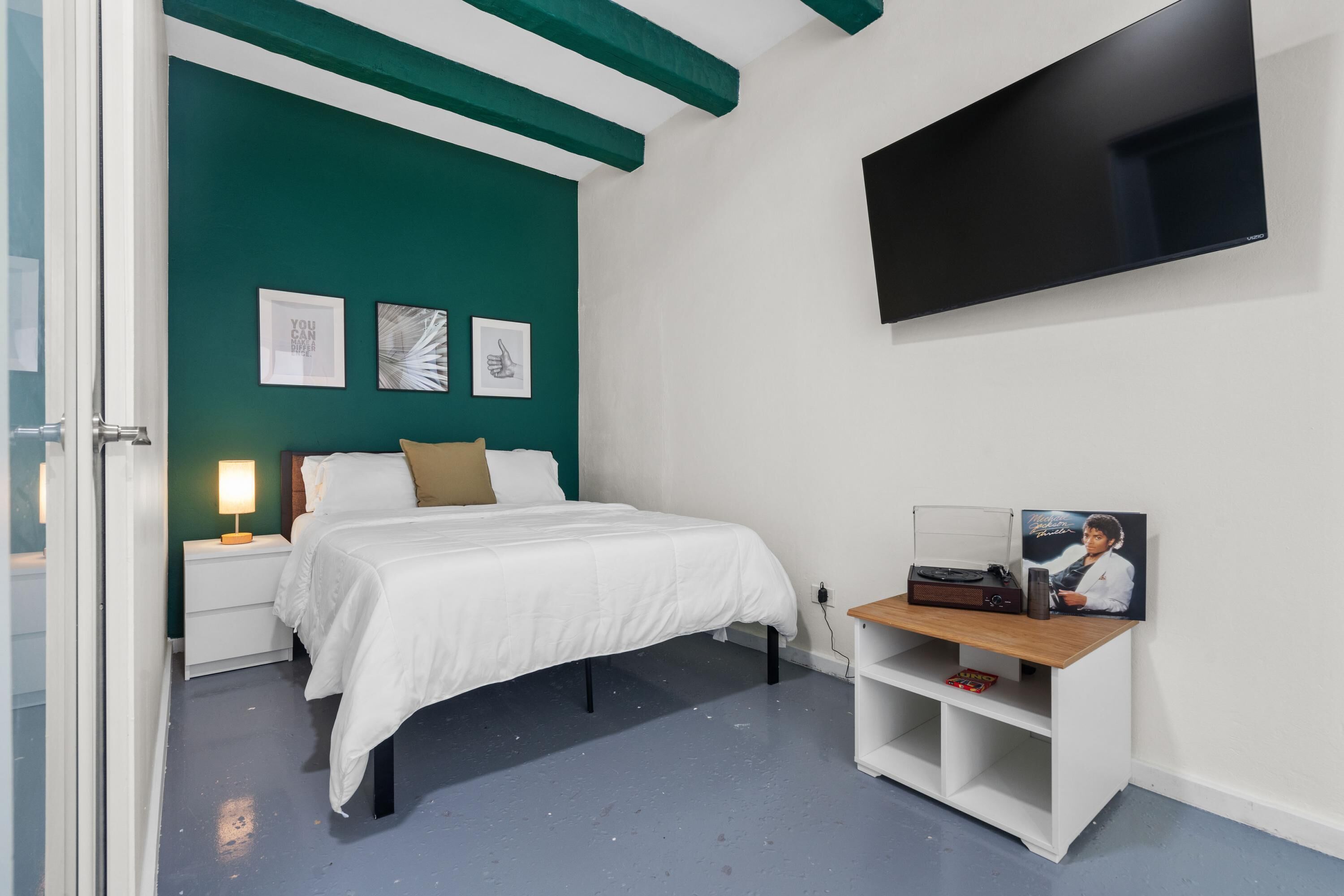 A bedroom with a bed, a nightstand, a TV, and a shelf with a picture frame and a book.