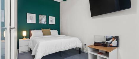 A bedroom with a bed, a nightstand, a TV, and a shelf with a picture frame and a book.