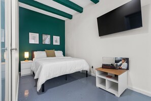 A bedroom with a bed, a nightstand, a TV, and a shelf with a picture frame and a book. - Otium Rentals Comfort Studio in Condado (San Juan)