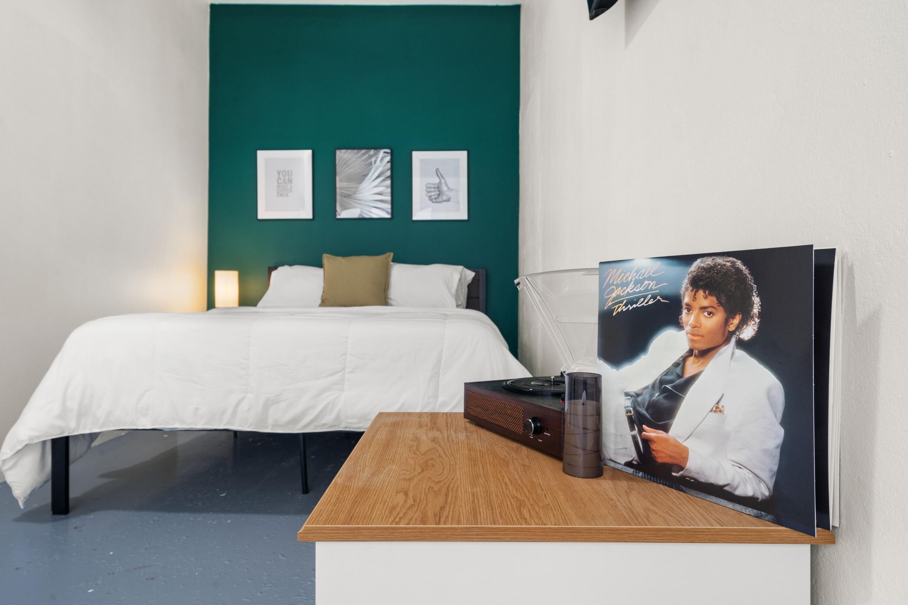 Quarto com cama, mesa de cabeceira de madeira e um pôster do Michael Jackson.